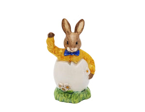 The bunny is waving as he pops out of an Easter egg wearing a bright yellow shirt and dark blue bow tie.