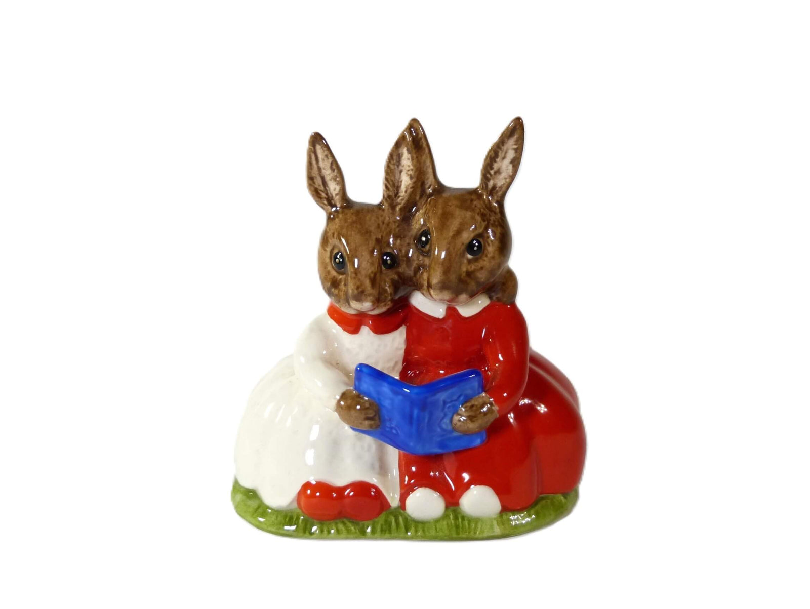 Two little girl Bunnykins, one in a red dress the other in a white dress, they are sitting reading a blue book.